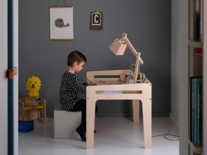 Ein Junge sitzt am YORI Kinderschreibtisch höhenverstellbar vor einer grauen Wand und hellgrauem Fussboden