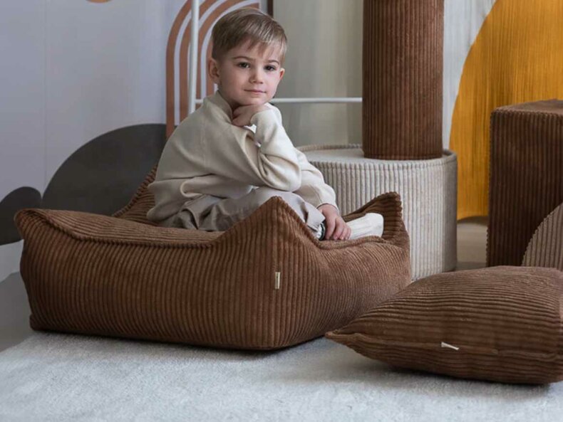 Ein Junge sitzt im Kinderzimmer auf dem XL Sitzkissen in Farbe toffee aus Kordstoff